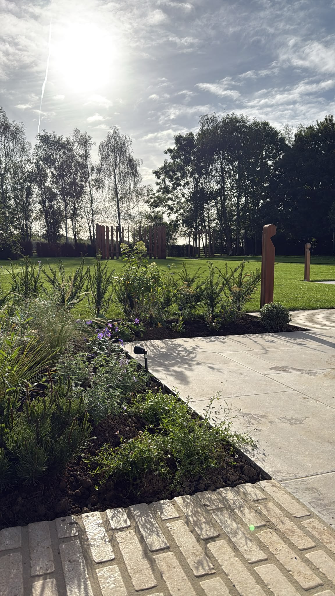 Patio, planting and timber posts across the lawn