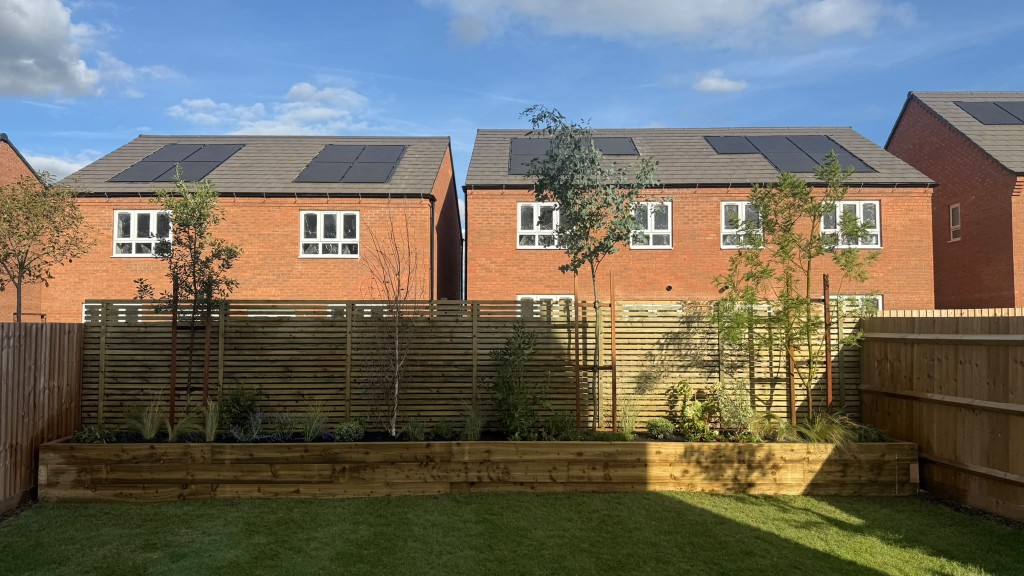 Long raised timber planter with mature trees and a slatted fence across the back of a new-build garden in Rothley